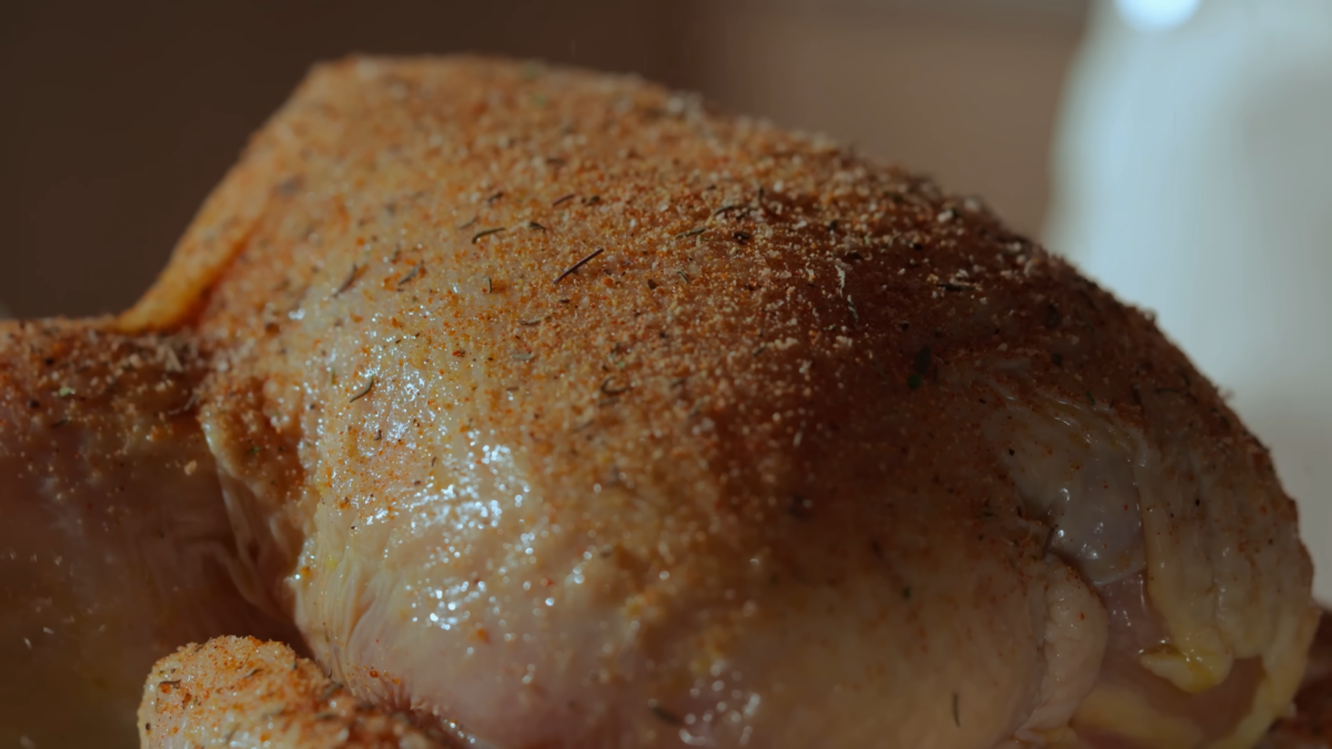 A whole raw chicken coated in oil and seasonings.