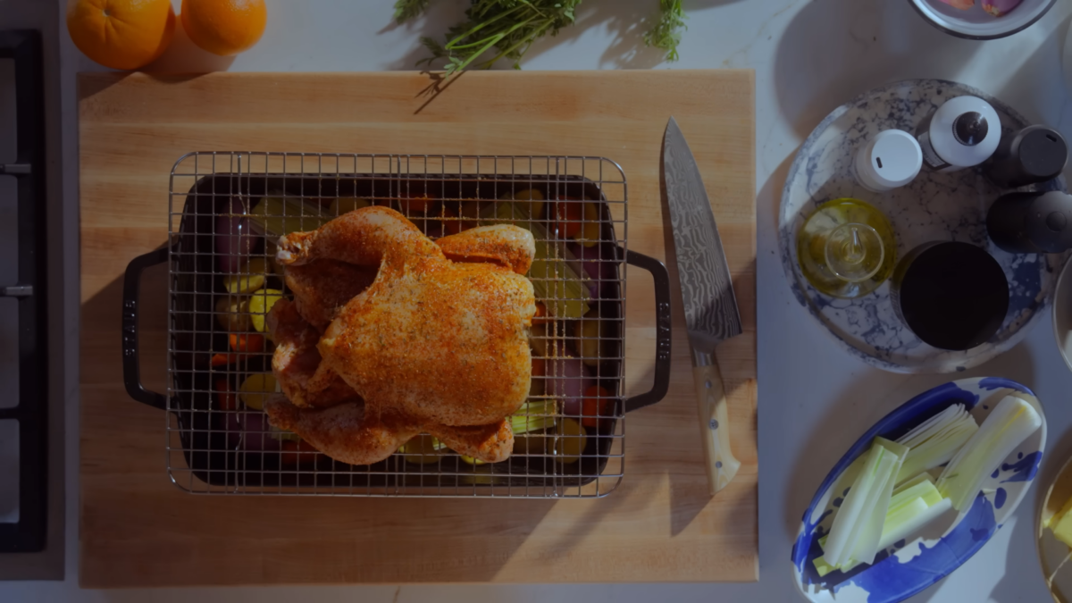 a whole chicken on a wire rack over top of a pan full of veggies.