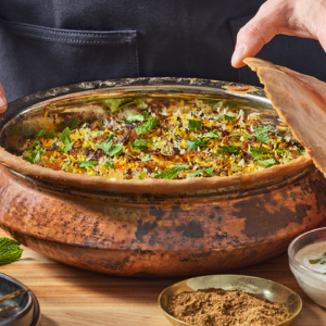 A pot of chicken biryani with the dough top leaning against the side.