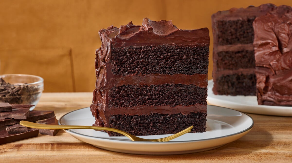 A slice of three layer chocolate layer cake on a plate with a fork.