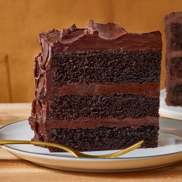 A slice of three layer chocolate layer cake on a plate with a fork.