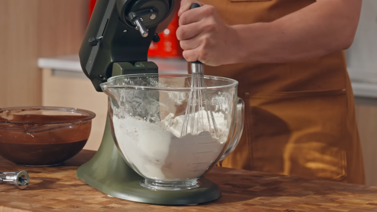A man whisking flour in a glass bowl.