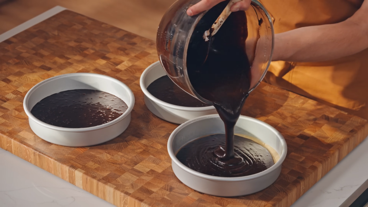A man pouring cake batter into separate cake tins.