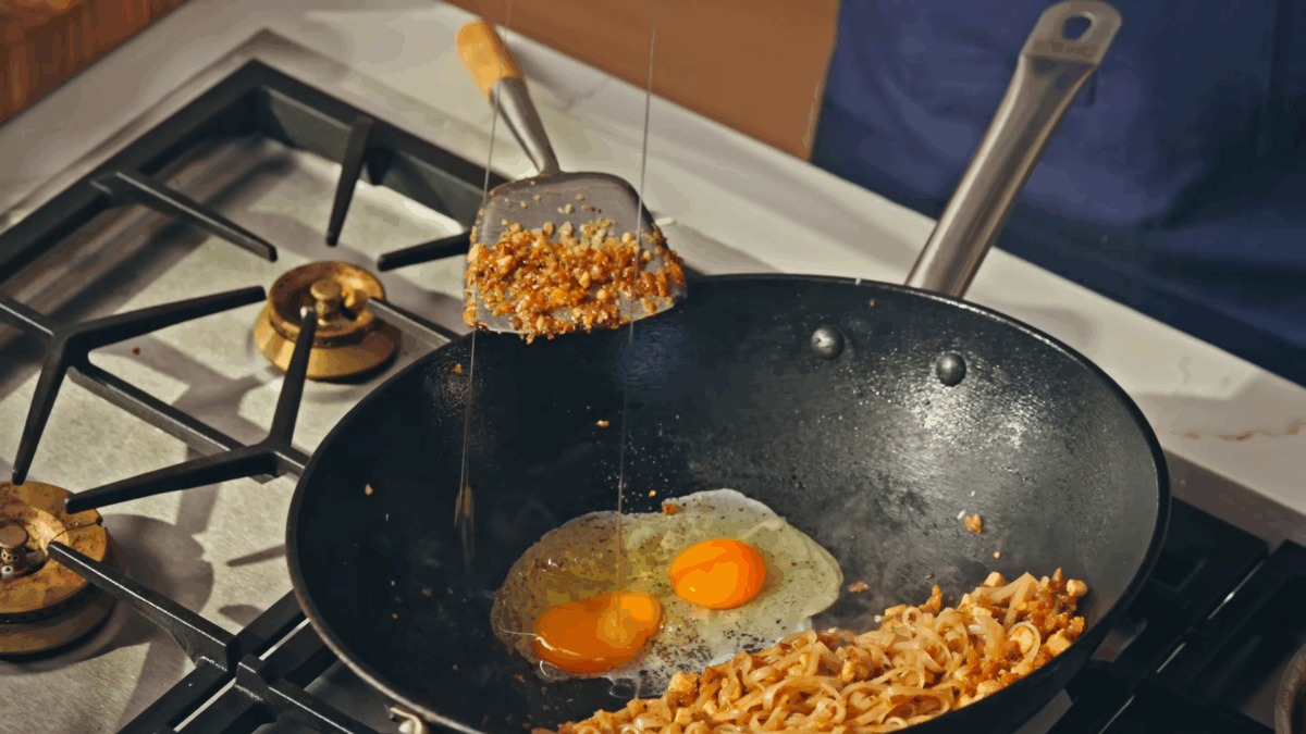 Pad Thai cooking in a wok with two freshly cracked eggs.