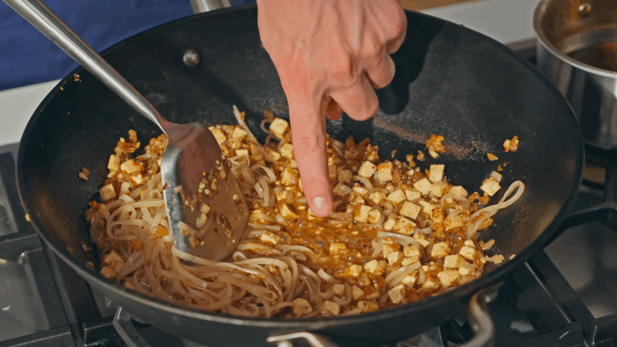 Pad Thai with rice noodles and cubed tofu cooking in a wok.