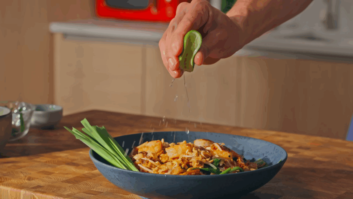 A man squeezing fresh lime juice over a bowl of pad Thai.