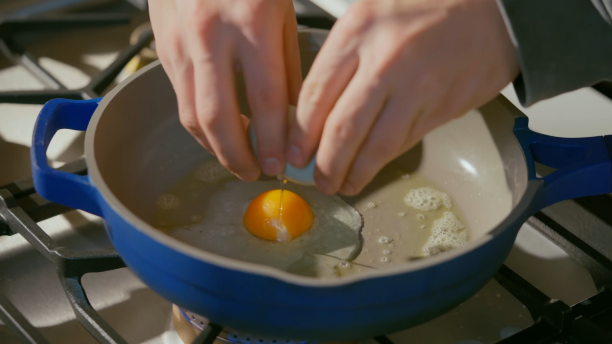 A man cracking an egg into a skillet.