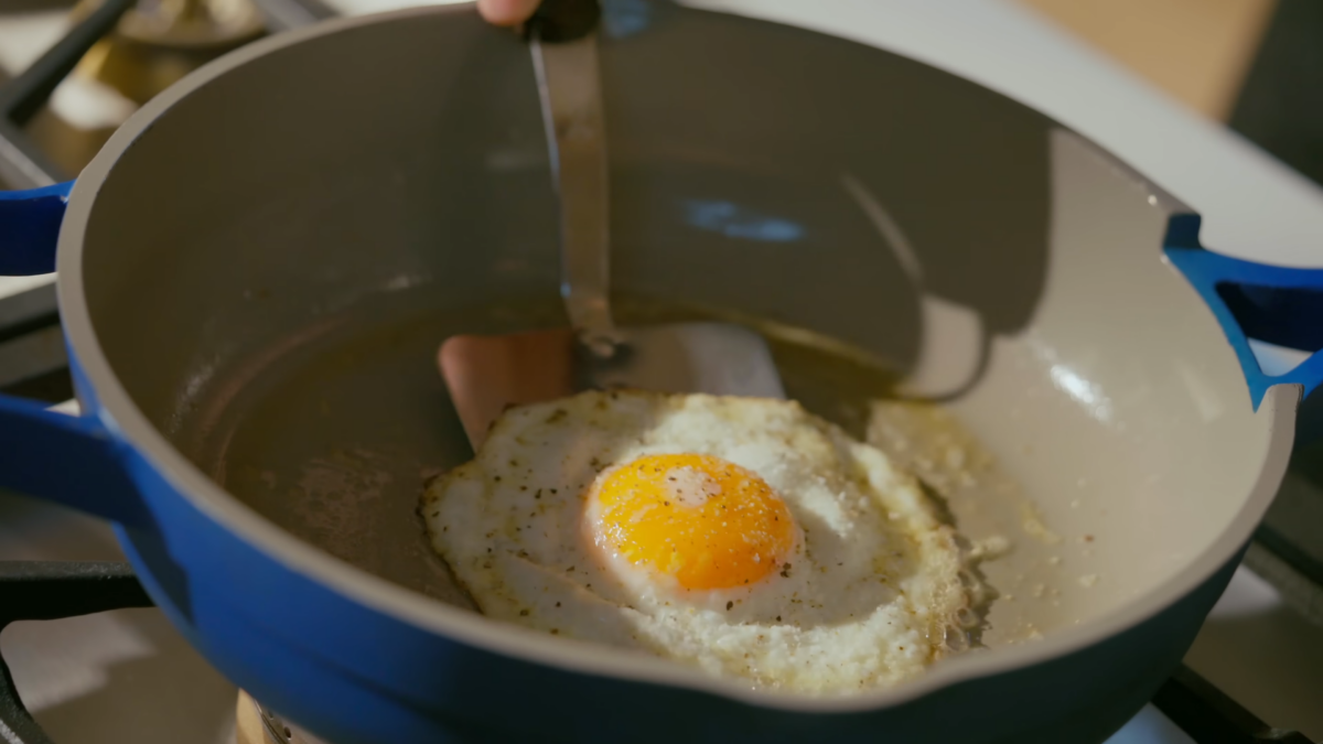 An egg cooking on a skillet about to be flipped with a metal spatula.
