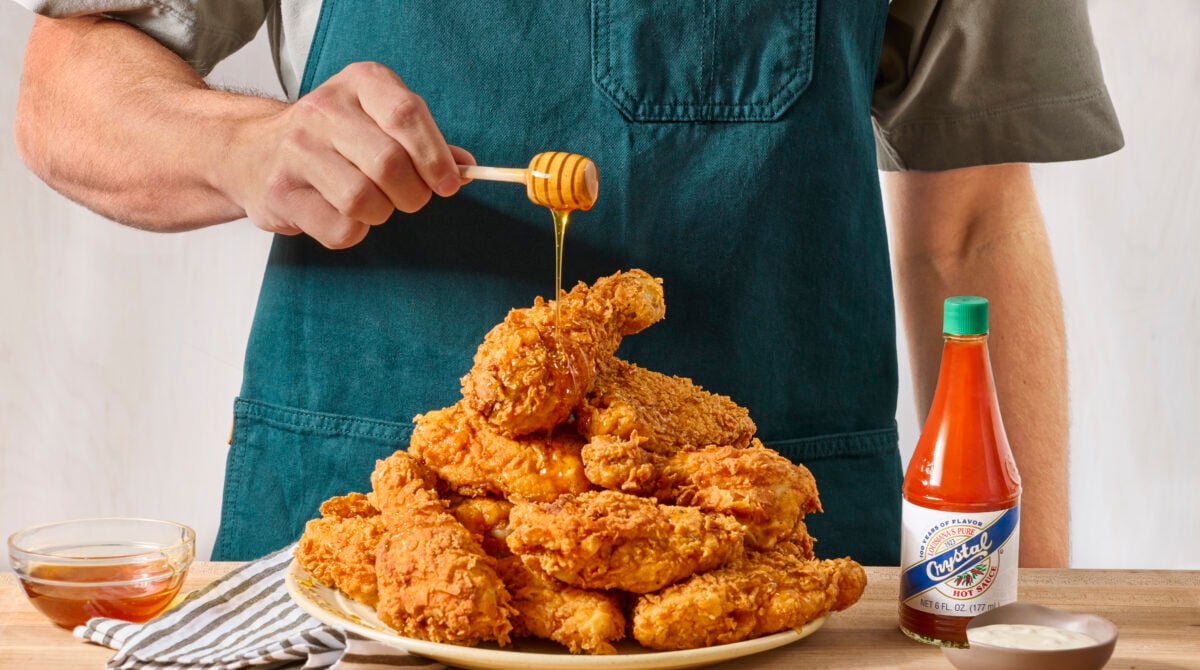 A man drizzling hot honey over a plate of buttermilk fried chicken.