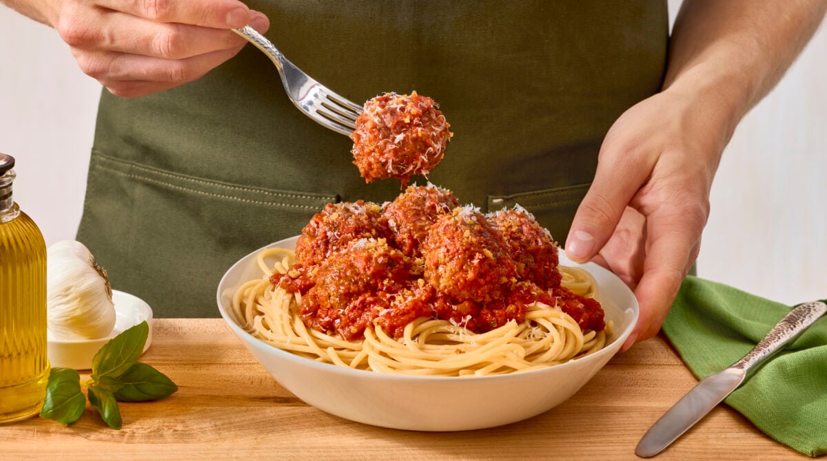 A fork holding a meatball above a bowl of spaghetti and meatballs.