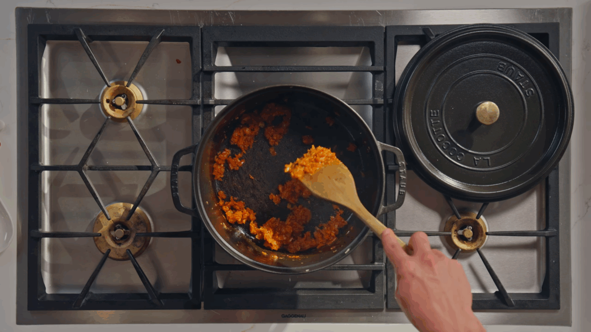 Tomato paste being stirred into a garlic and onion mixture.