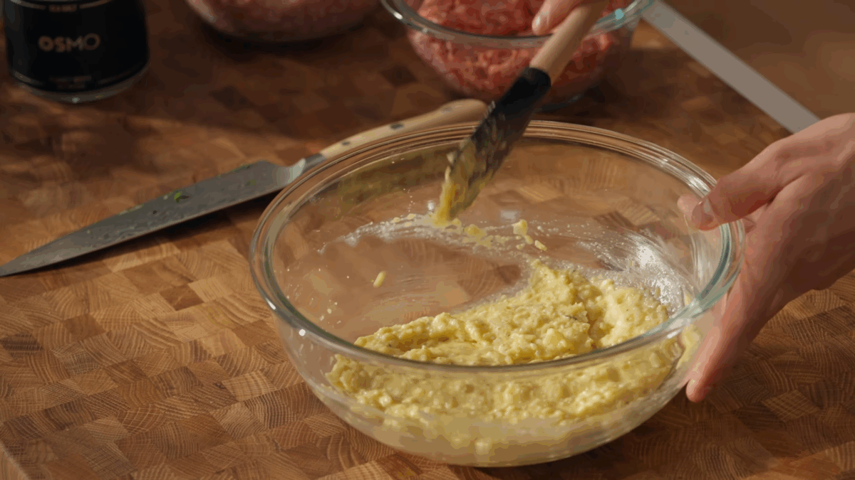 Breadcrumbs, milk, cheese, eggs, onions, and garlic being whisked.