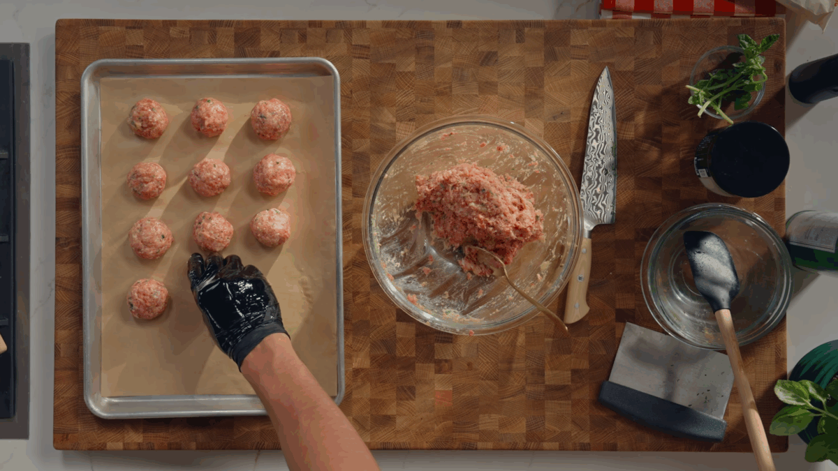 Raw meatballs being portioned and placed on a sheet tray.