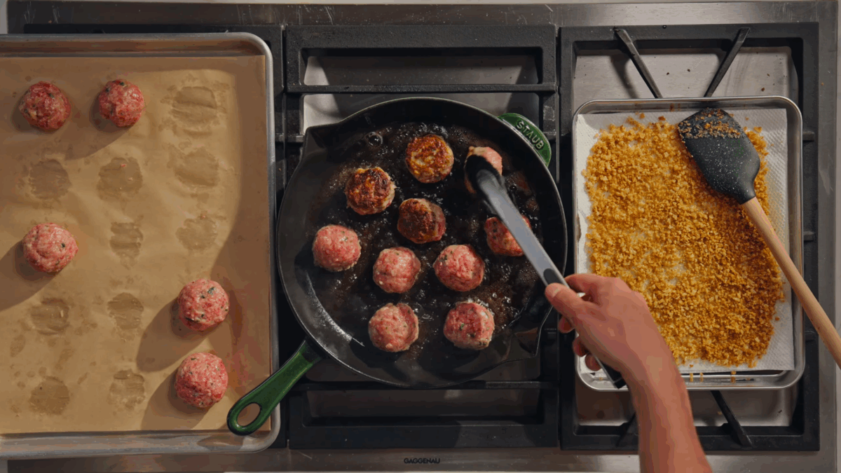 Meatballs searing in a skillet.