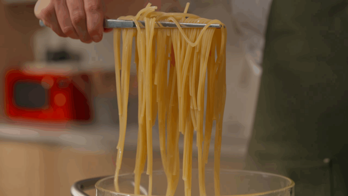 Cooked spaghetti being lifted from a pot of water.