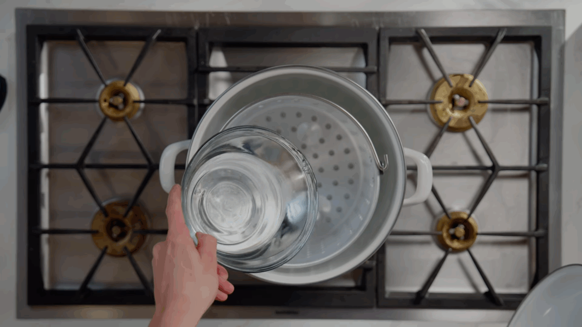 Water being poured into a pot with a steamer basket.