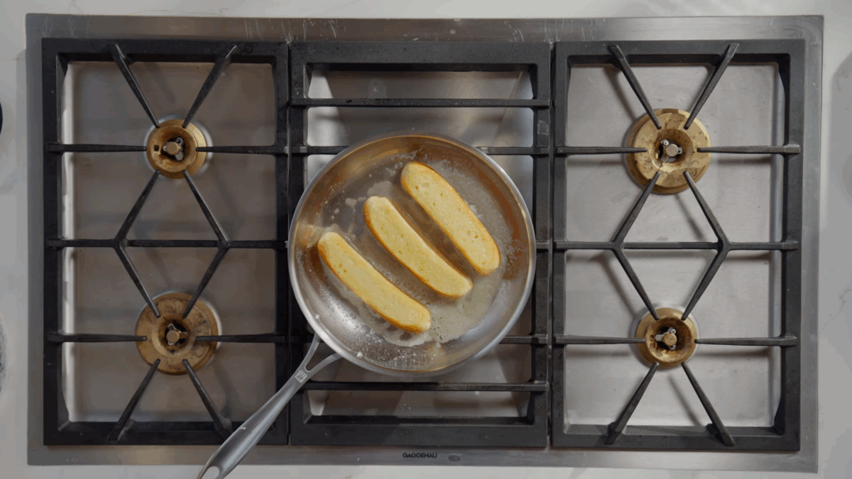 Three New England style buns toasting in butter in a skillet.