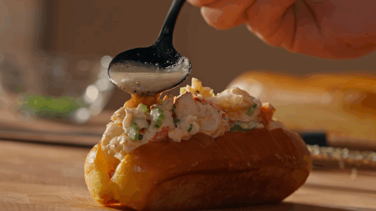 Brown butter being drizzled over a lobster roll.