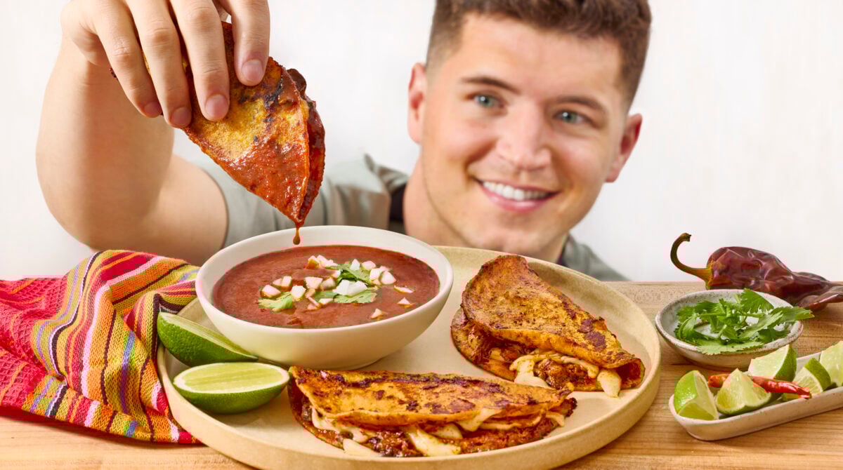 A man dipping a beef birria taco into a bowl of consomé.