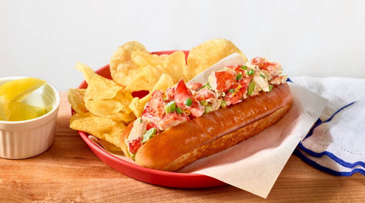 A lobster roll in a red basket with potato chips.