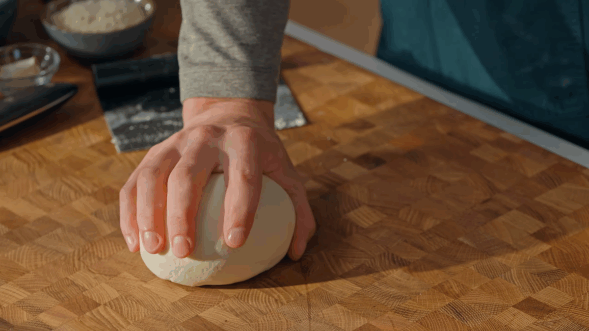Pasta dough being kneaded on a wooden work surface. 