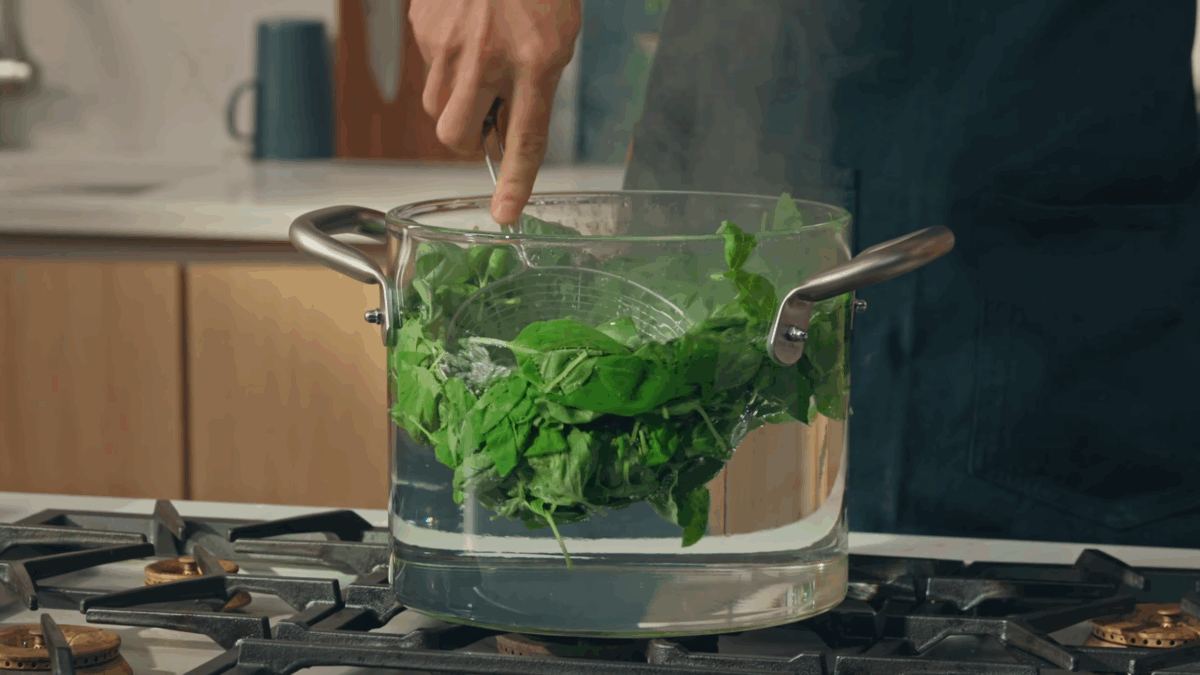 Basil being blanched in a pot on the stove. 