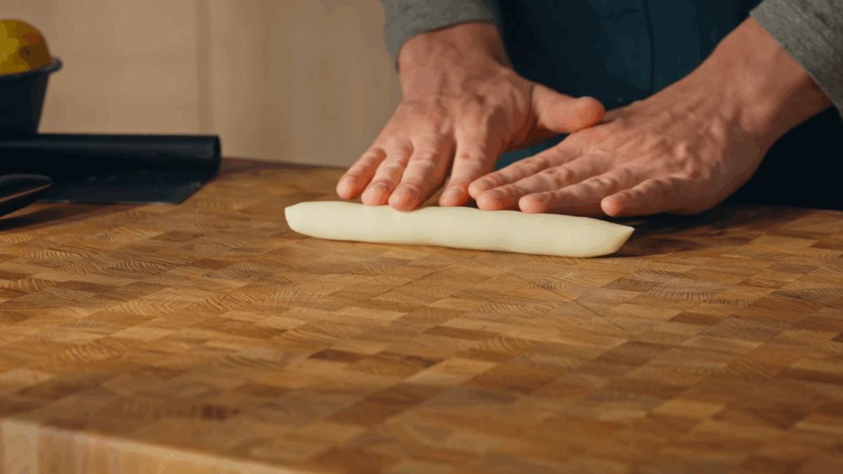 Pasta dough being rolled on a wooden surface. 