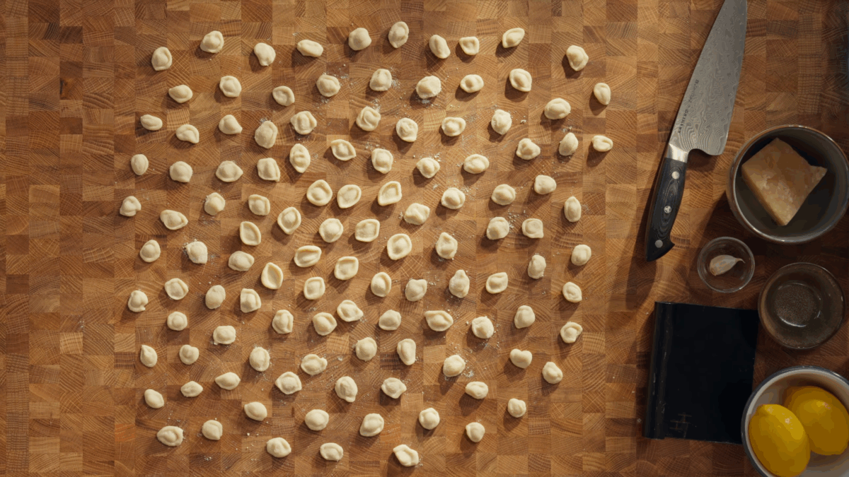 Uncooked orecchiette pieces on a wooden work surface. 