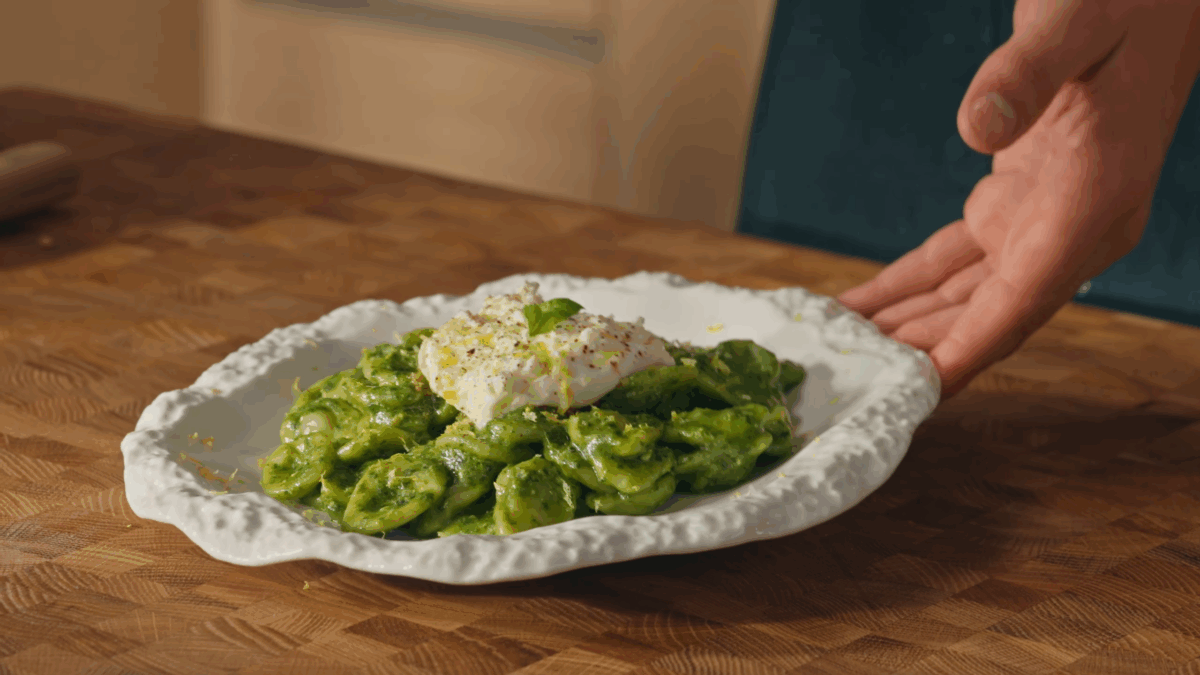 Basil pesto pasta being plated with toppings. 