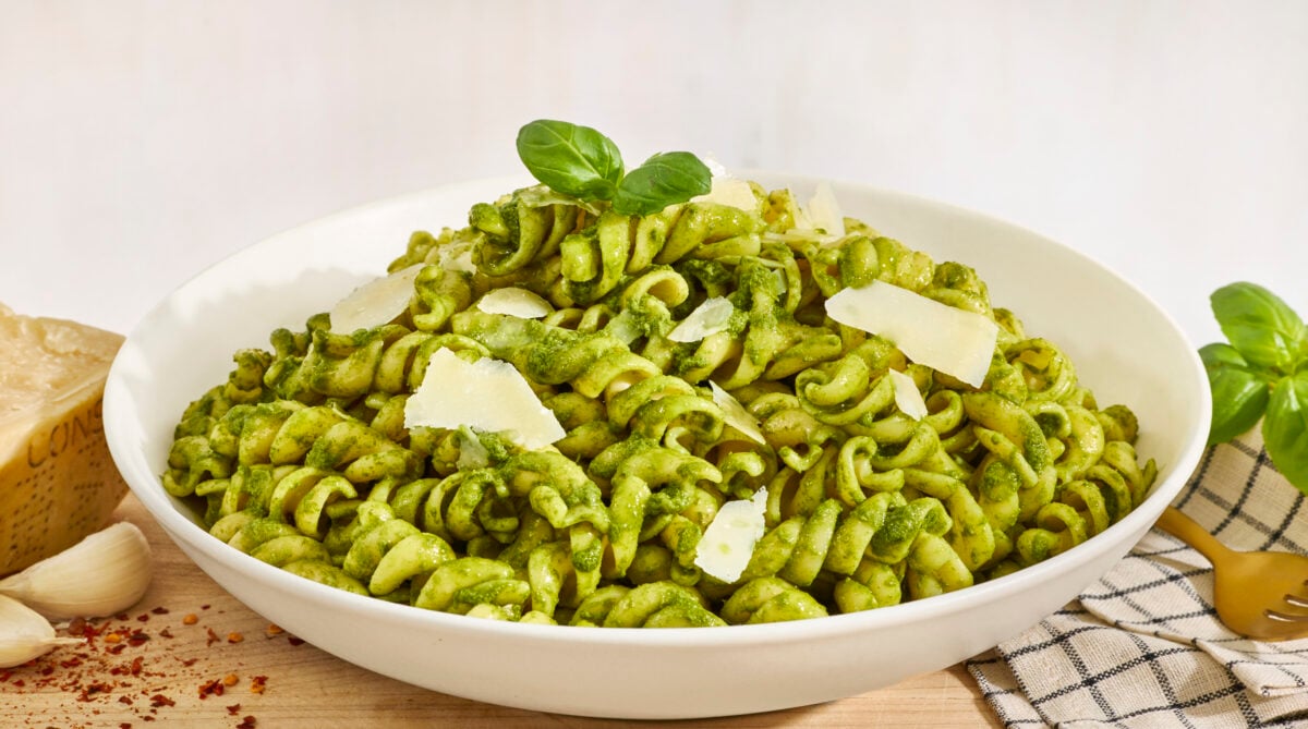 A bowl of basil pesto pasta topped with shaved Parmesan cheese and fresh basil. 