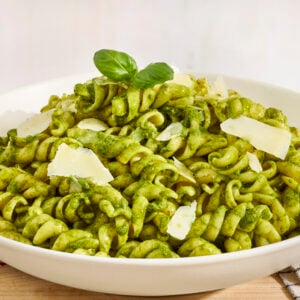 A white shallow bowl filled with pesto pasta.