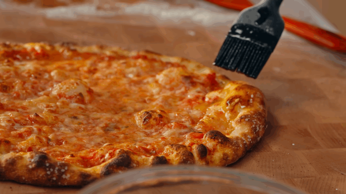 Butter being brushed over a baked New York style pizza. 