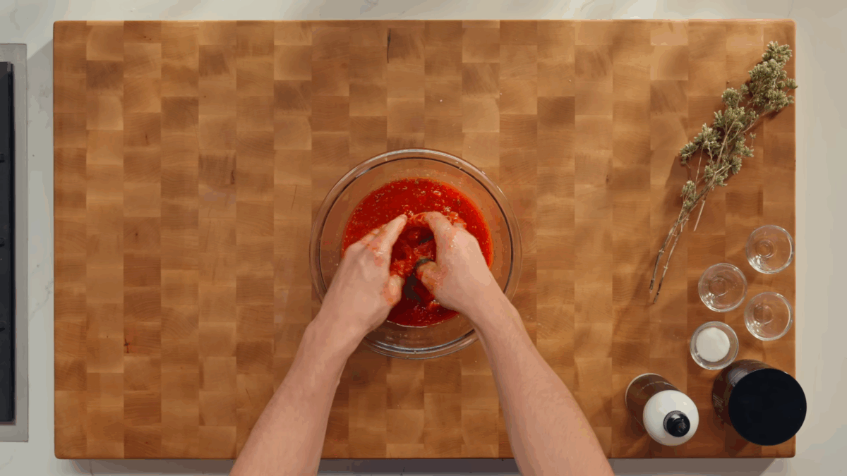 A bowl of tomatoes being crushed with two hands. 