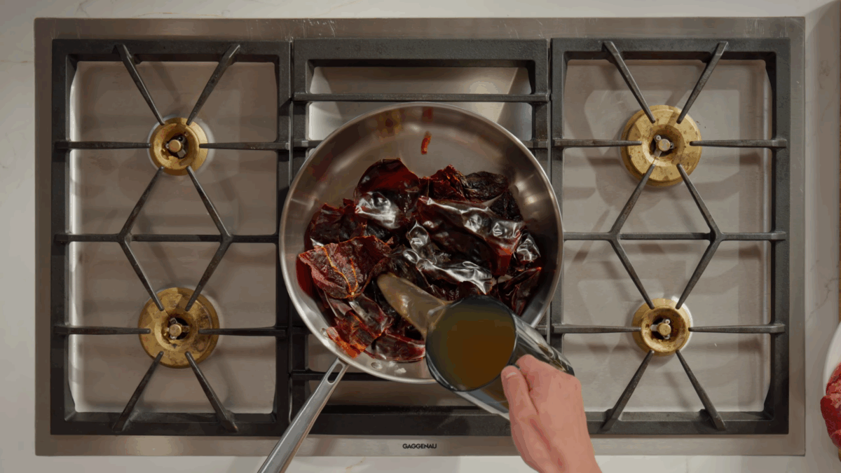 Beef stock being poured into a skillet with chiles.