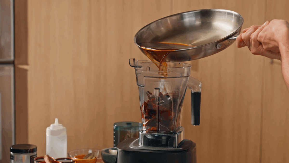 Beef stock being poured into a blender with chiles.