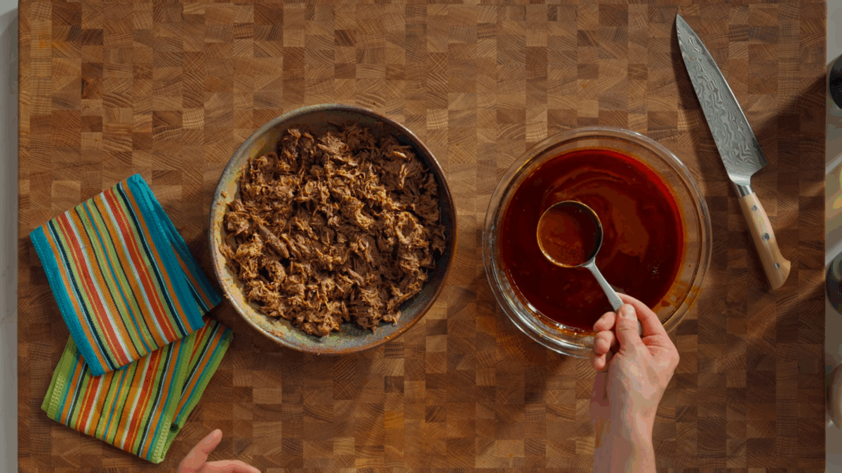 A bowl of shredded beef birria and a bowl of consomé sauce.