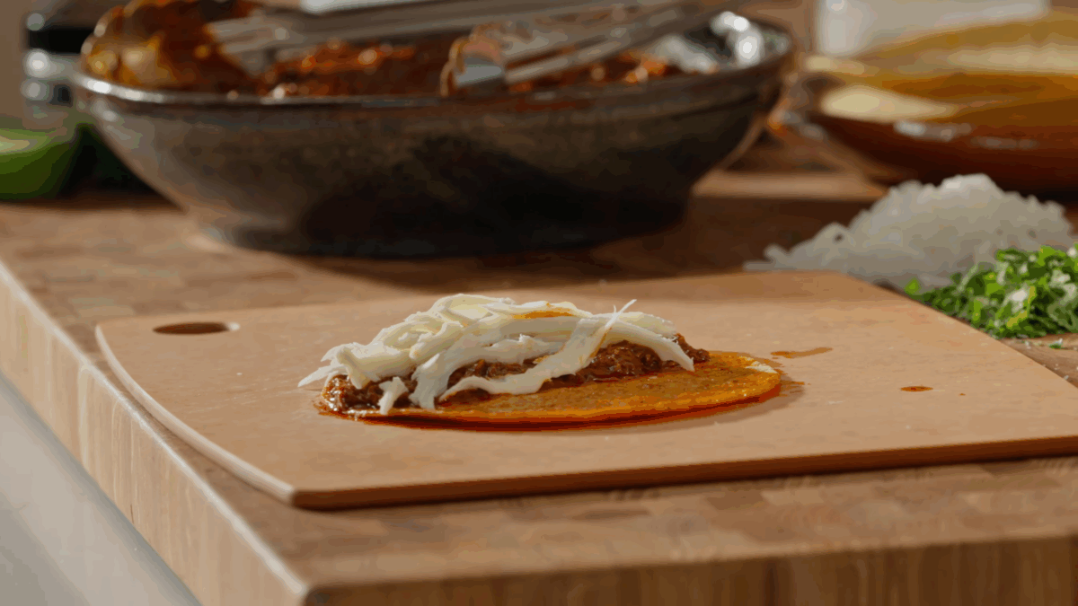 An open-faced beef birria taco on a cutting board.