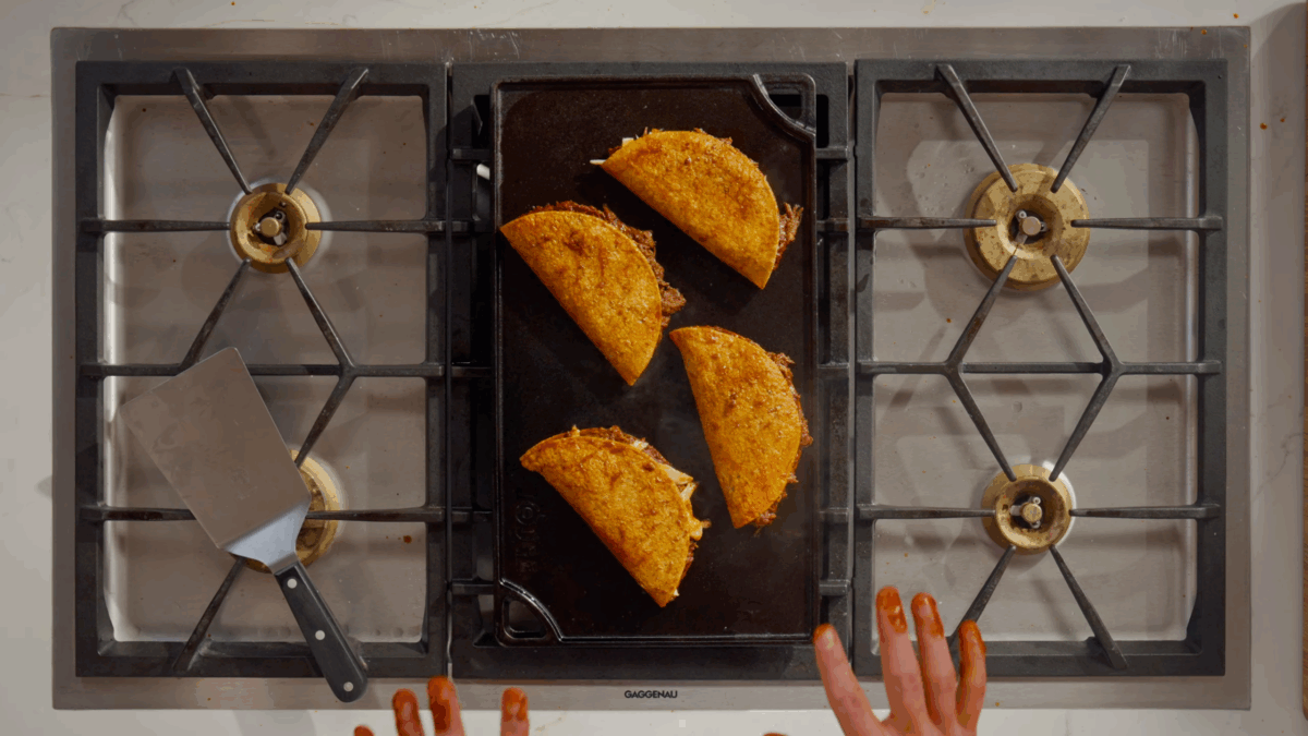 Four beef birria tacos cooking on a stovetop.
