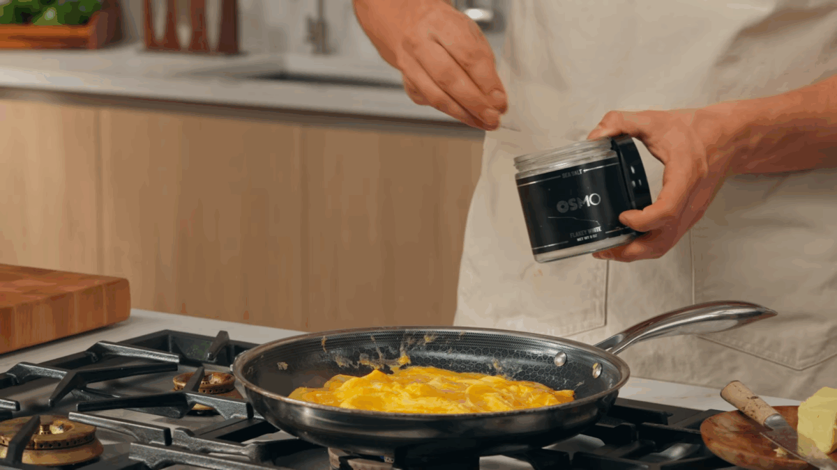 Scrambled eggs being seasoned with salt in a skillet. 