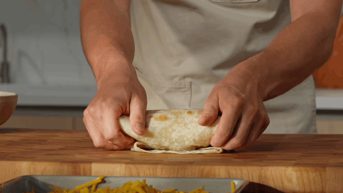 A breakfast burrito being rolled with two hands. 