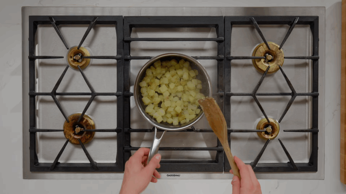 Boiled potatoes being lightly toasted in a pot on the stove.
