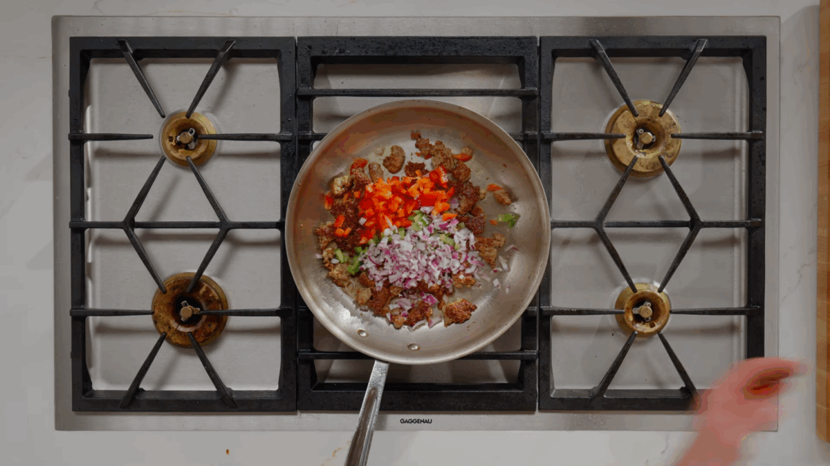 Peppers, onions, and sausage in a skillet on the stove. 