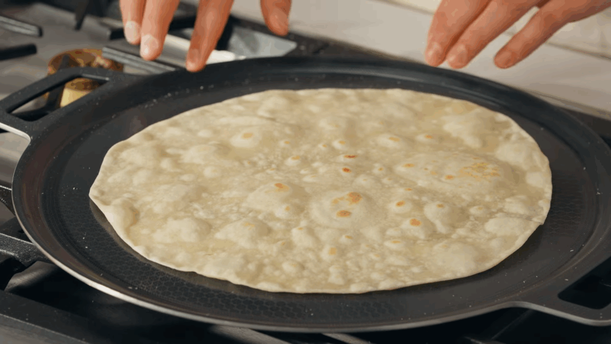 A homemade tortilla cookking on a pan.