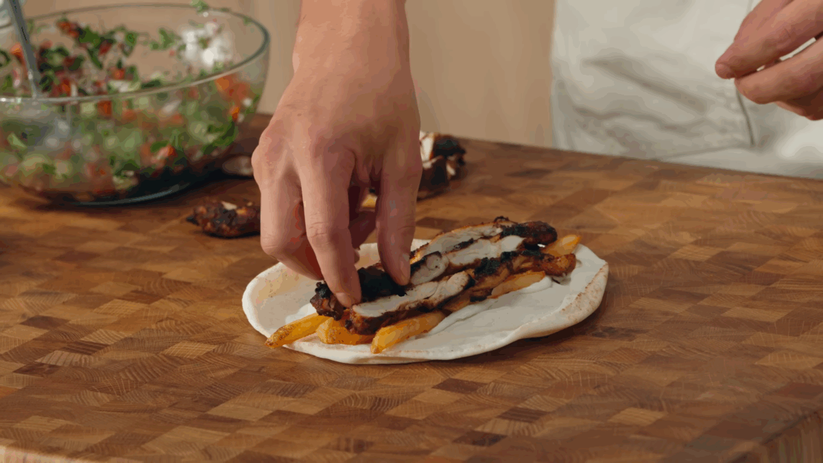 French fries and chicken being layered over pita bread.