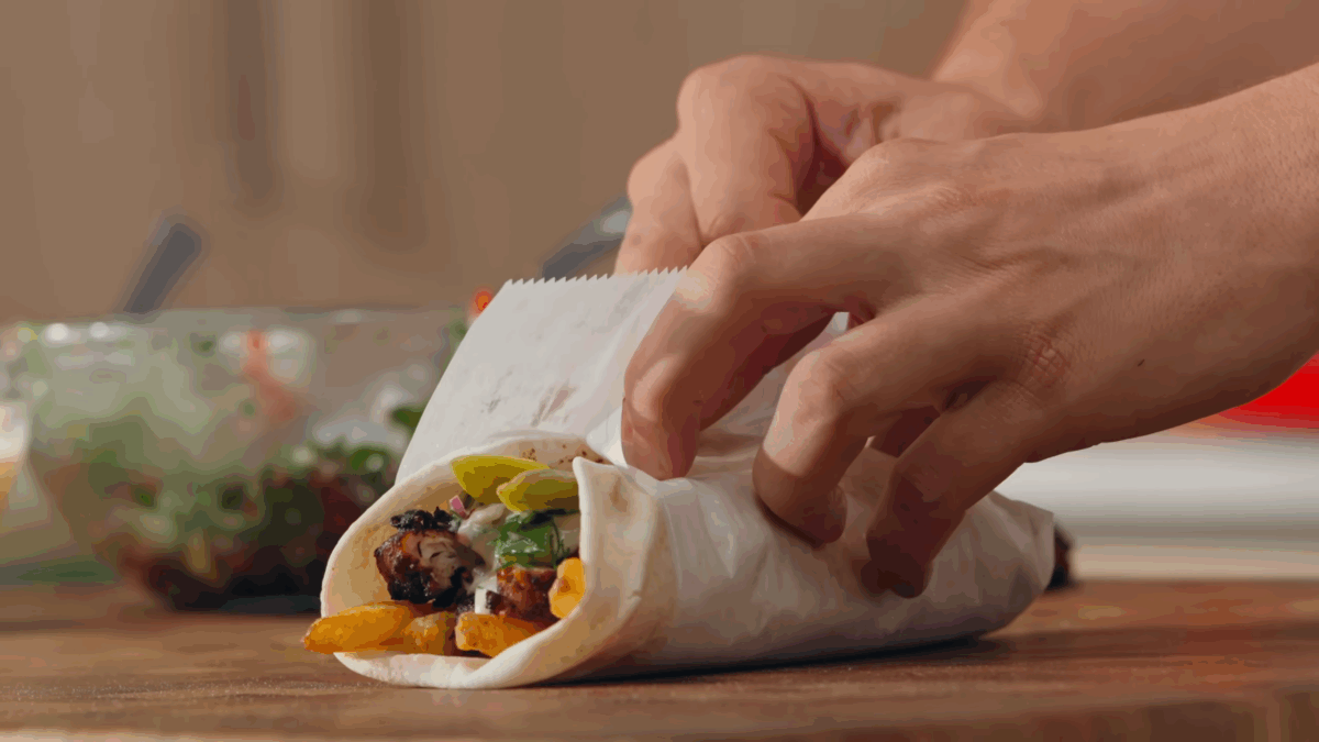 A chicken shawarma wrap being wrapped with parchment paper.
