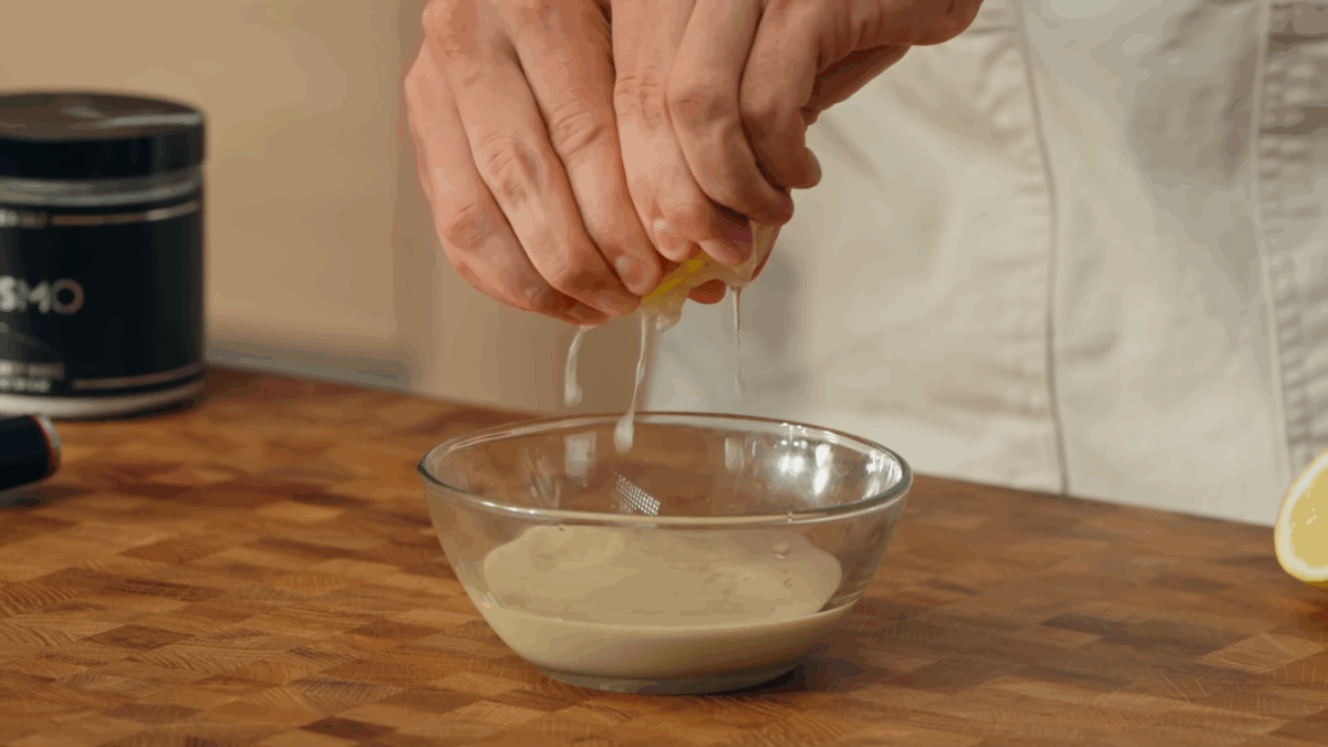 Lemon juice being squeezed into a bowl of tahini sauce.