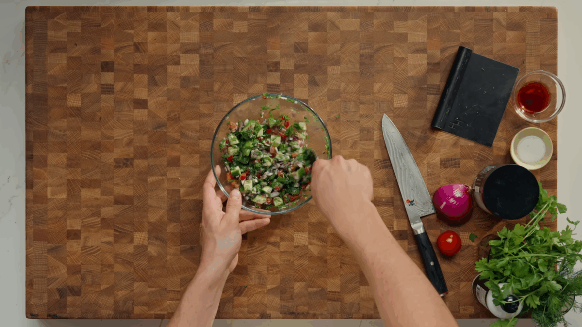 Cucumber and tomato salad being tossed in a bowl.