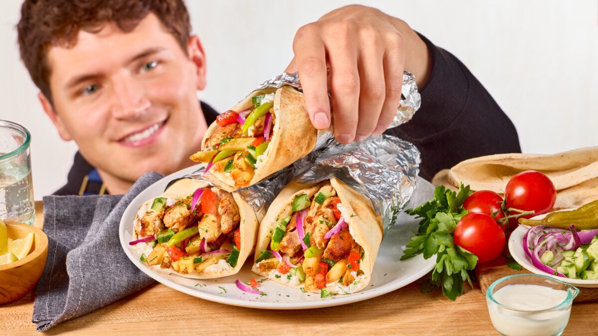 Nick DiGiovanni grabbing a chicken shawarma wrap from a plate.