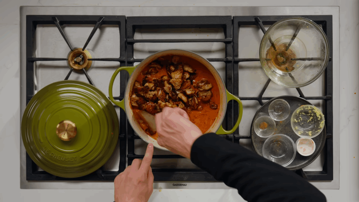 Cooked chicken being stirred into a pot of butter chicken sauce.