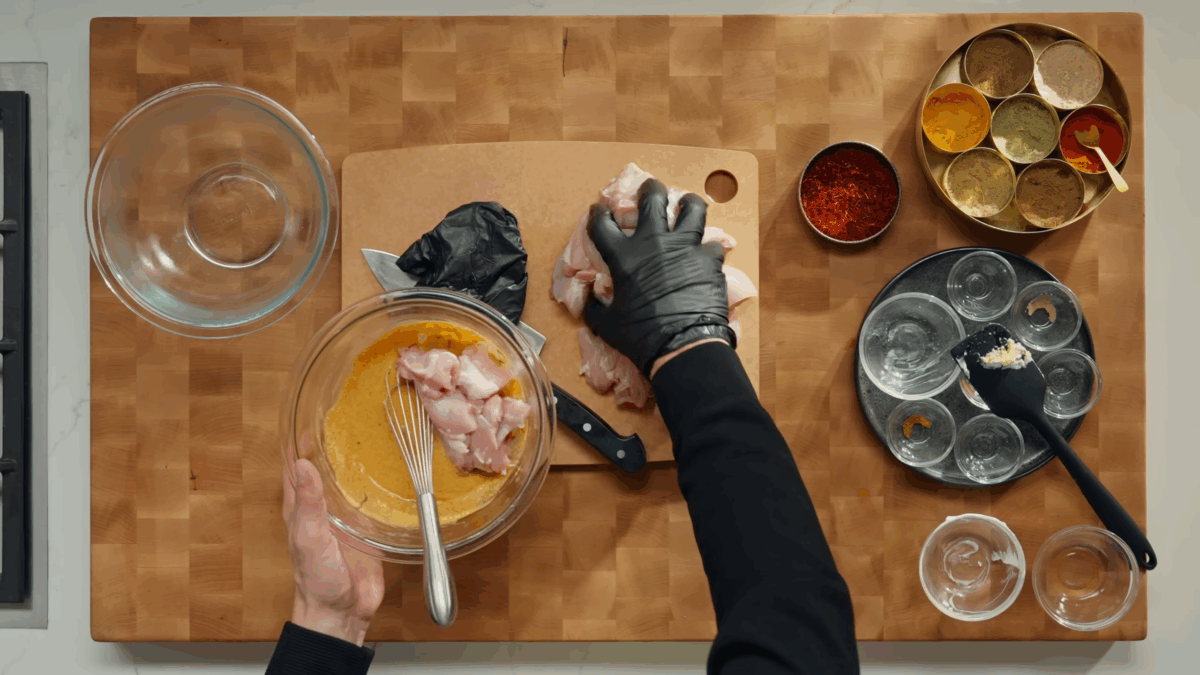 Raw chicken thighs being added to butter chicken marinade.